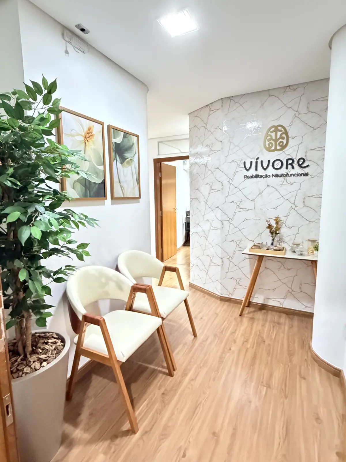 Recepção da Vívore, com poltronas, planta e a marca na parede