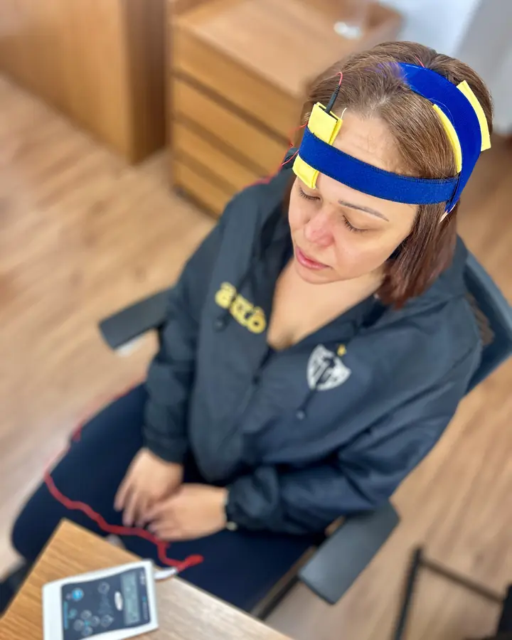 Paciente sentada durante sessão de tDCS, com a faixa de eletrodos na cabeça